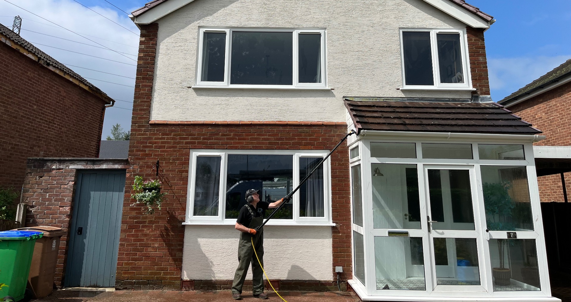 A Unique Exterior Cleaning technician cleaning gutters with a water-fed pole at a brick and rendered home with a glazed front porch